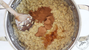 Cinnamon, peanut butter and honey added to cooked oats in a pot.