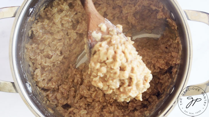 A wooden spoon lifts some Peanut Butter Oatmeal out of a pot.