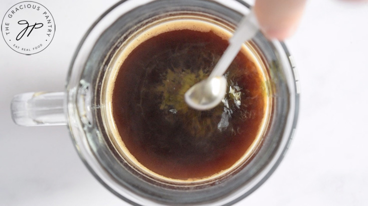 A measuring spoon adding peppermint extract to a mug of coffee.