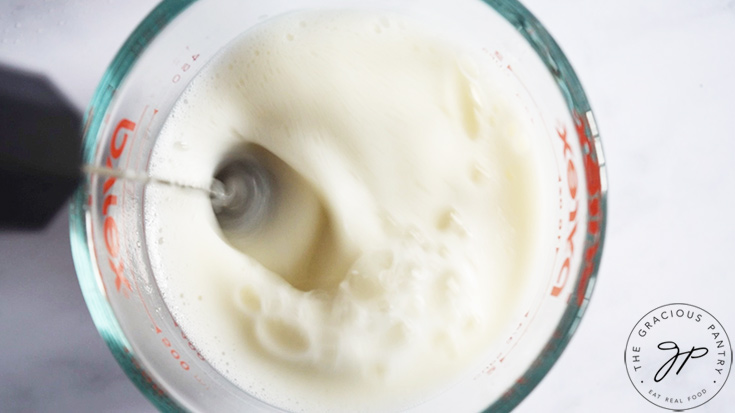 Milk being frothed in a glass measuring cup.