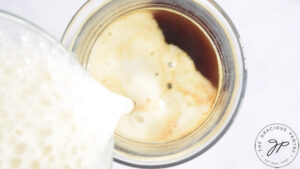 Pouring frothed milk into a glass mug of coffee.