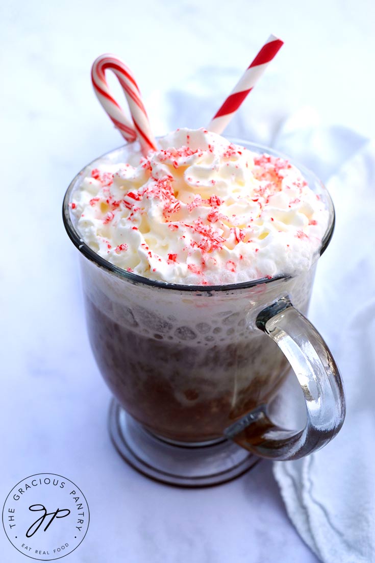 A glass mug filled with peppermint latte and topped with whipped cream, crushed candy cane and a whole candy cane for garnish.