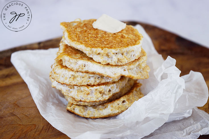 A stack of protein pancakes sitting on a piece of parchment paper with a pat of butter on top of the stack.