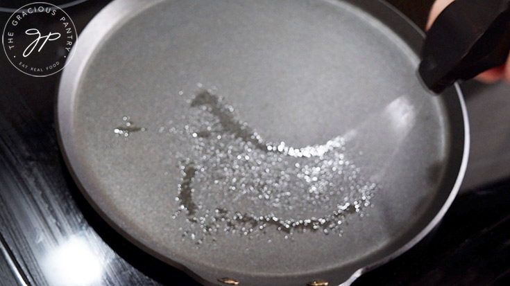 A skillet being sprayed with an oil sprayer.