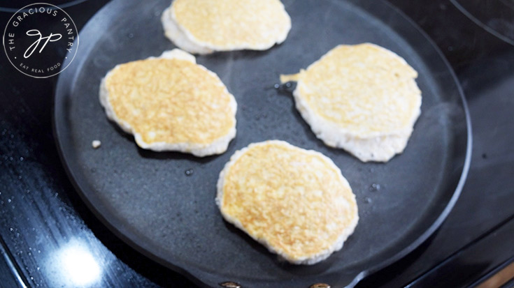 4 golden protein pancakes cooking on a skillet.