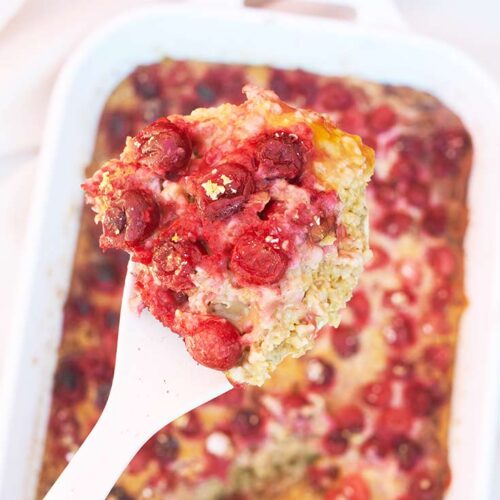 A spoons lifts a serving of Pumpkin Baked Oatmeal out of a white casserole dish.