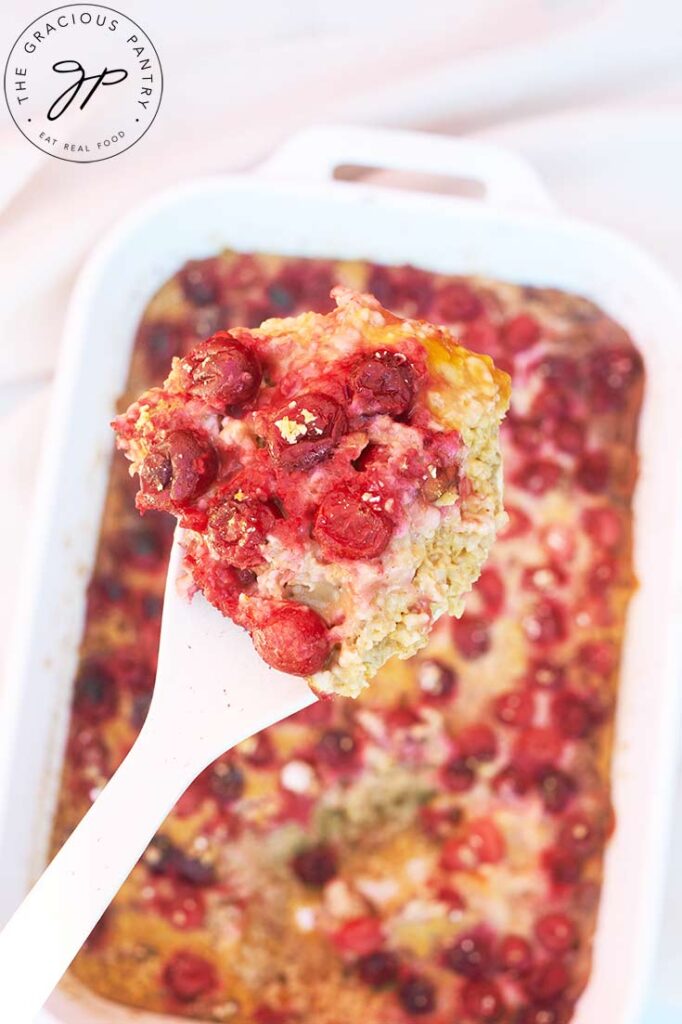 A spoons lifts a serving of Pumpkin Baked Oatmeal out of a white casserole dish.