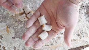 A hand holds up a few raw, cut gnocchi.