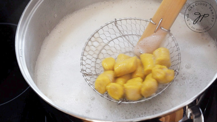 Lifting cooked pumpkin gnocchi out of boiling water with a slotted spoon.