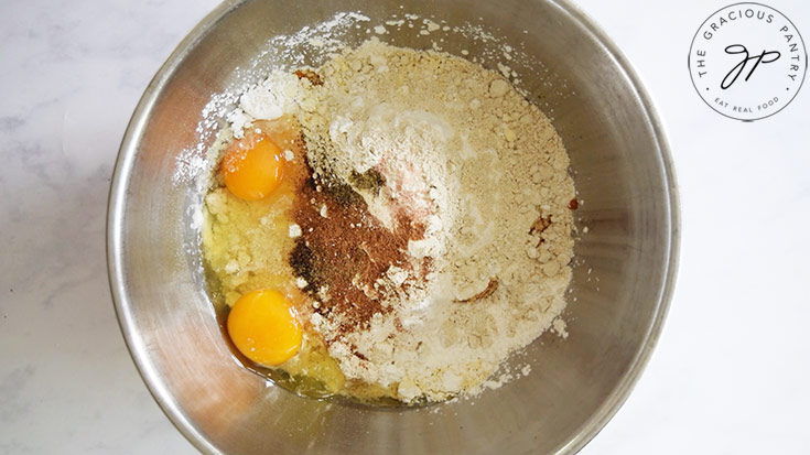 Eggs and spices added to pumpkin pureé and flour in a metal mixing bowl.