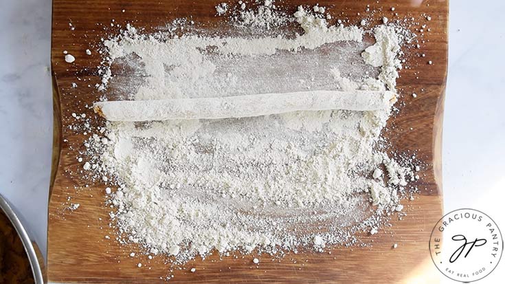 A rolled cord of Pumpkin Gnocchi dough on a floured work surface.