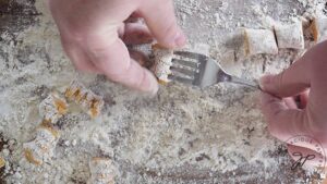 A gnocchi being shaped on the back of a fork.