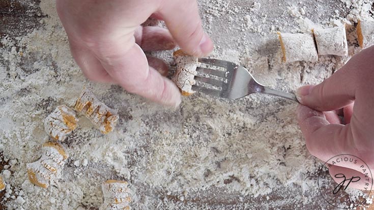 A gnocchi being shaped on the back of a fork.
