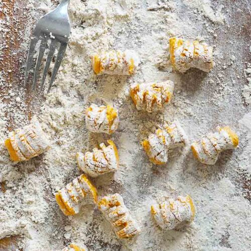 Just-made Pumpkin Gnocchi rest on a cutting board in flour.