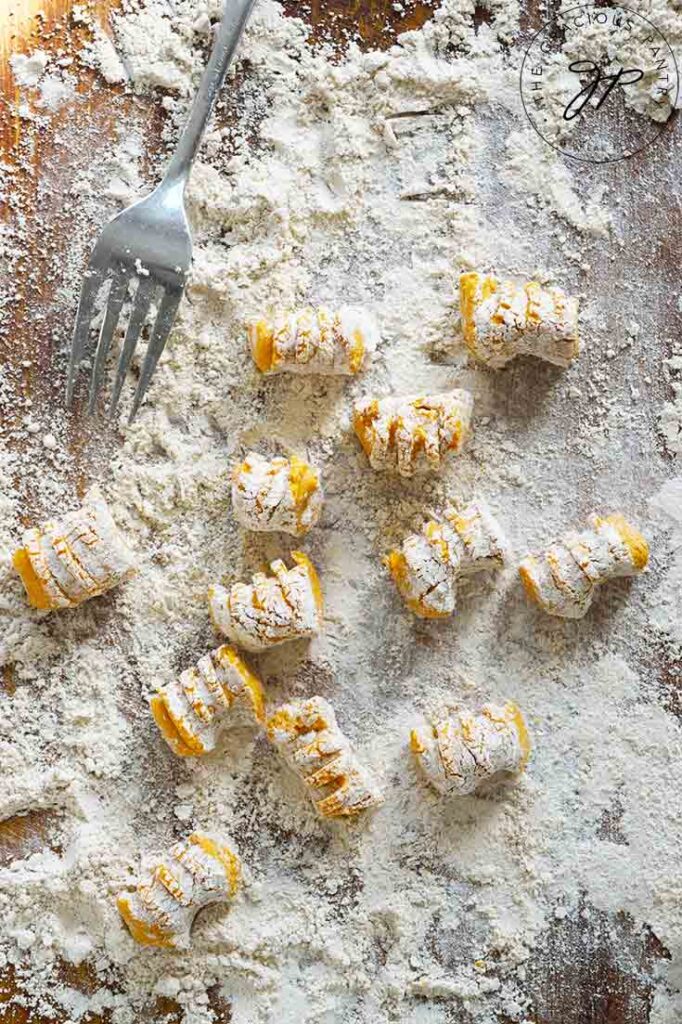 Just-made Pumpkin Gnocchi rest on a cutting board in flour.