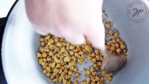Stirring chickpeas and seasonings in a mixing bowl to combine everything.