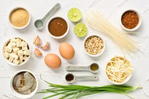 Ingredients for this Shrimp Pad Thai Recipe in individual, white bowls, sitting on a white surface.