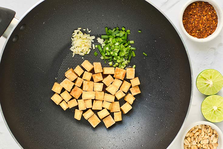 Cooked tofu cubes with chives and garlic sitting in a wok.