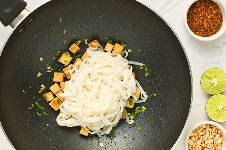 Cooked rice noodles and tofu sitting in a wok.