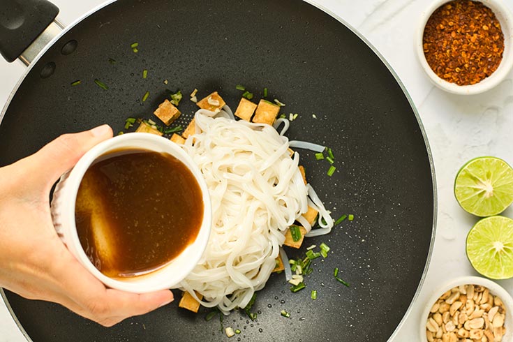 Adding pad thai sauce to a wok filled with tofu and rice noodles.