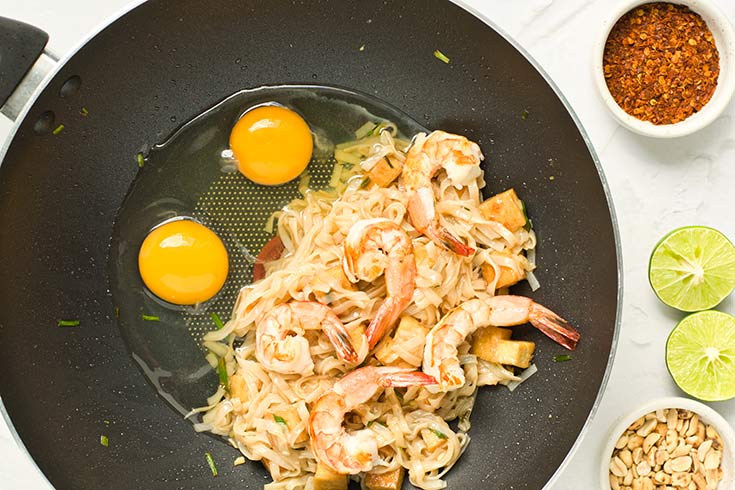 Two raw eggs sitting in a wok next to pad thai.