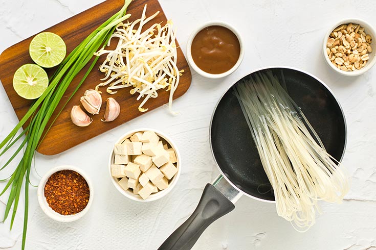 Rice noodles placed in a pot of water for cooking with other ingredients sitting next to the pot.