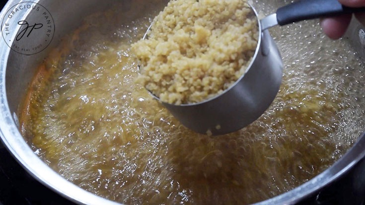 Cooked quinoa being added to a pot of boiling broth.
