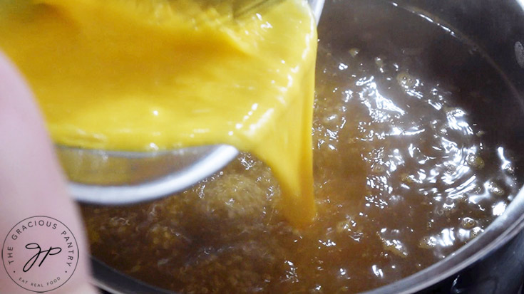 Whisked egg being added to boiling broth in a pot.