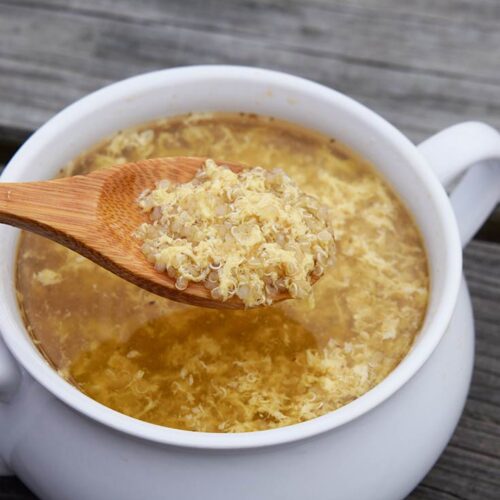 A spoon lifts a bit of sick day soup out of a white bowl.