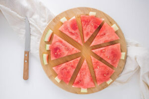8 Watermelon Christmas Tree triangles on a cutting board with the rind cut away to form the tree trunks on each piece.