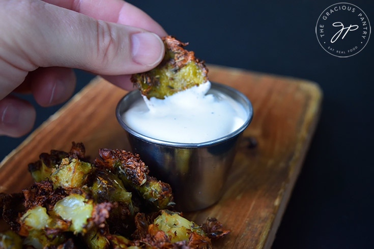 Air Fryer Smashed Brussels Sprouts piled onto a cutting board. One is being dipped in ranch dressin.