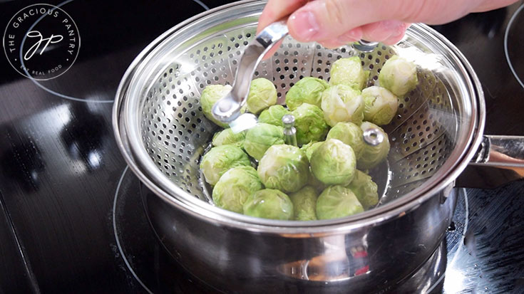Pouring raw brussels sprouts into a steamer pot.