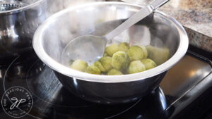 Transferring just-cooked brussels sprouts to a mixing bowl.