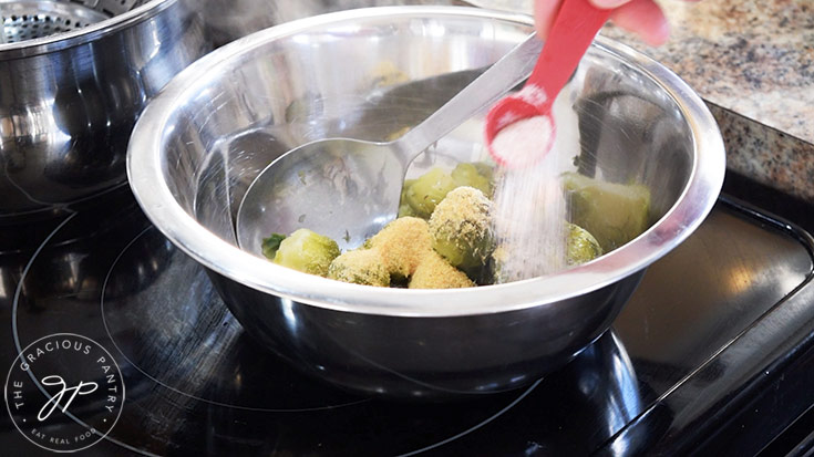 Adding spices to brussels sprouts in a mixing bowl.