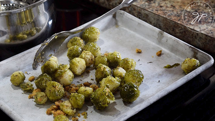 Pouring seasoned brussels sprouts onto a cookie sheet.