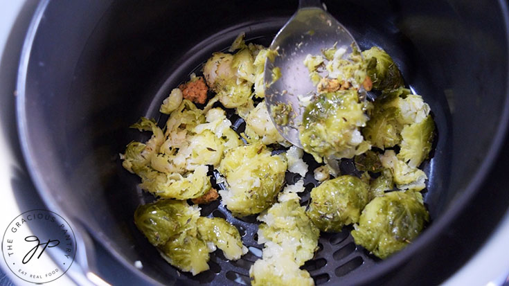 Placing smashed brussels sprouts into an air fryer basket.