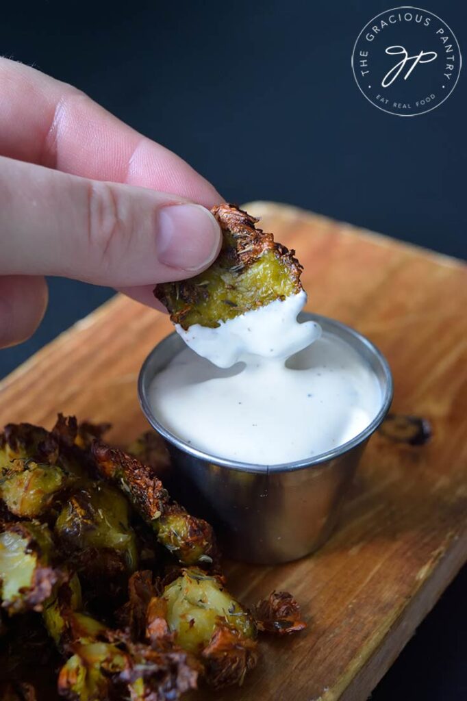 A hand dipping an Air Fryer Smashed Brussel Sprout into ranch dip.