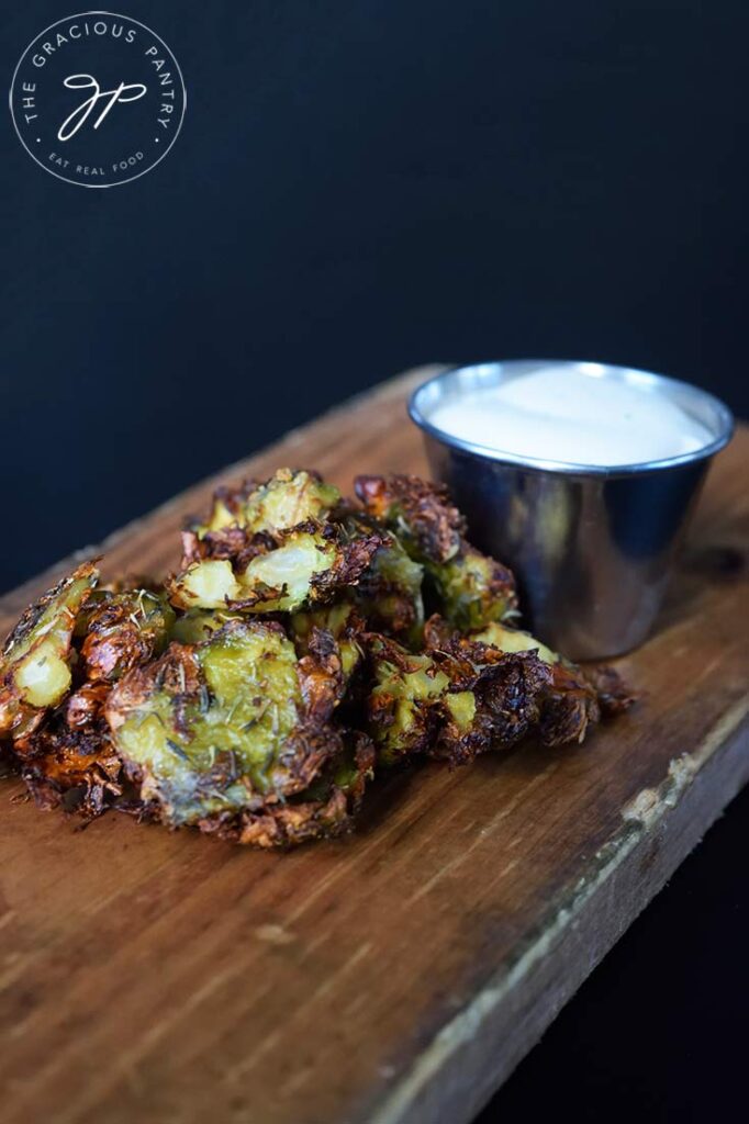 A pile of Air Fryer Smashed Brussels Sprouts on a cutting board in front of a dip cup full of ranch dressing.