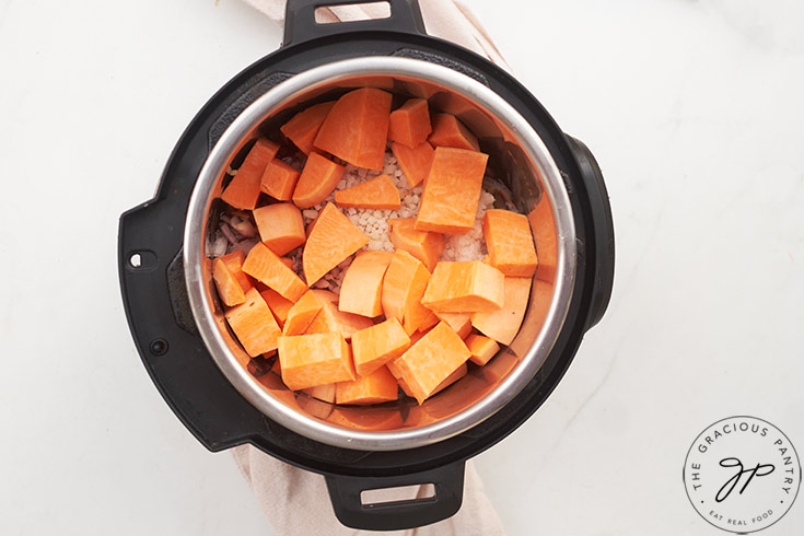 Riced cauliflower and chunks of raw sweet potato sitting in an Instant Pot.
