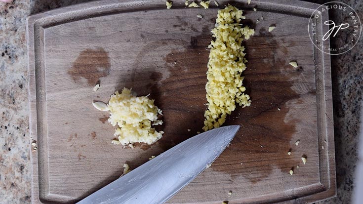 Pressed garlic and minced, fresh ginger on a wooden cutting board.