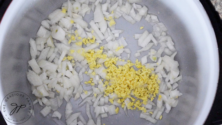 Minced ginger and pressed garlic added to onions in a pot.