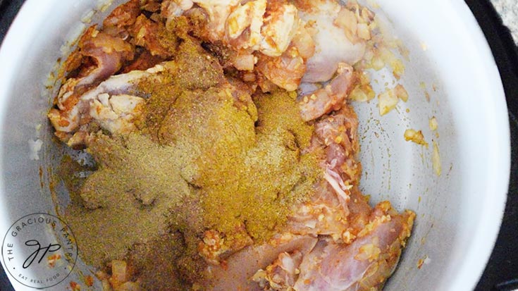 Spices added to raw chicken in a pot.