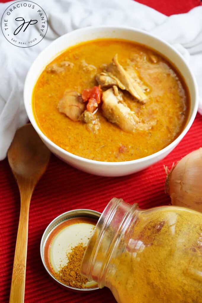 A side view of a white bowl filled with chicken curry soup. A wooden spoon rests to the left of the bowl.