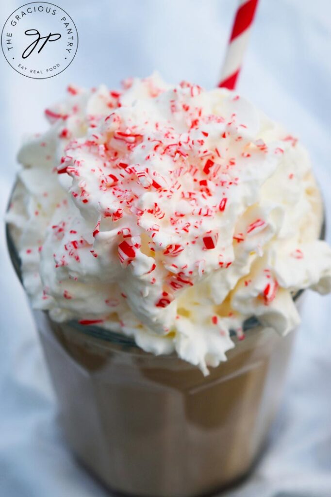 A close up of a Homemade Peppermint Mocha topped with whipped cream, crushed candy cane and a stripped straw.