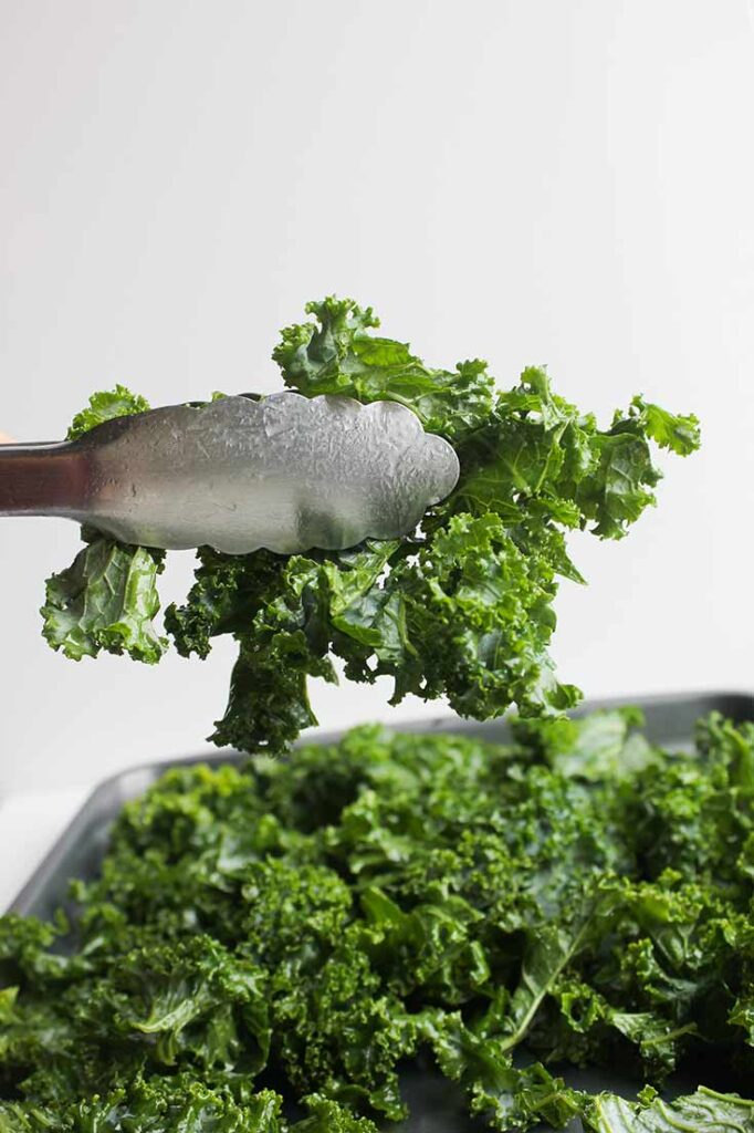 Tongs lifting a bunch of kale from a pile of it.