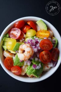 Mixed shrimp and avocado salad in a white bowl on a black background.