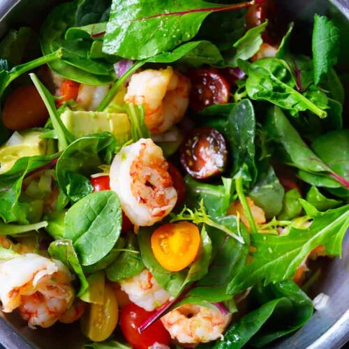 Shrimp and avocado salad mixed with greens in a mixing bowl.