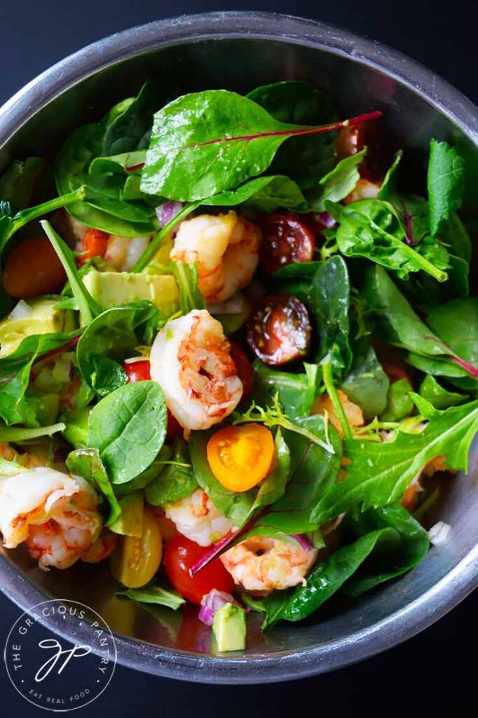 Shrimp and avocado salad mixed with greens in a mixing bowl.