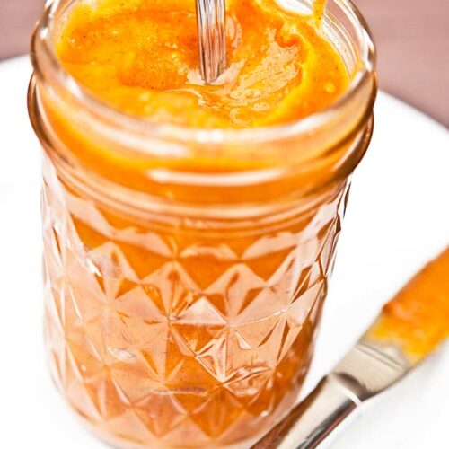 Sweet Potato Butter in a glass jar with the lid off and a spoon handle sticking out of it.