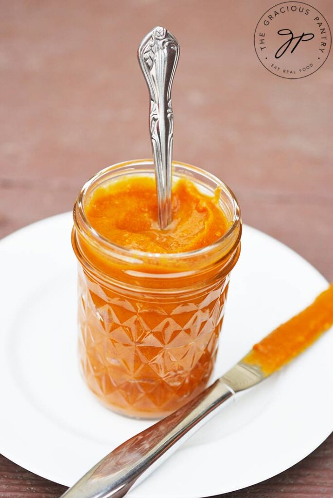 A spoon stands upright in a glass jar filled with Sweet Potato Butter.